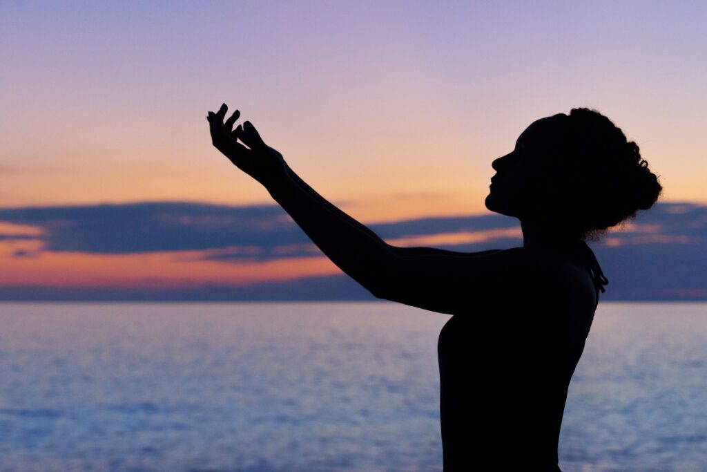 Lady with arms up in front of water with purple sky