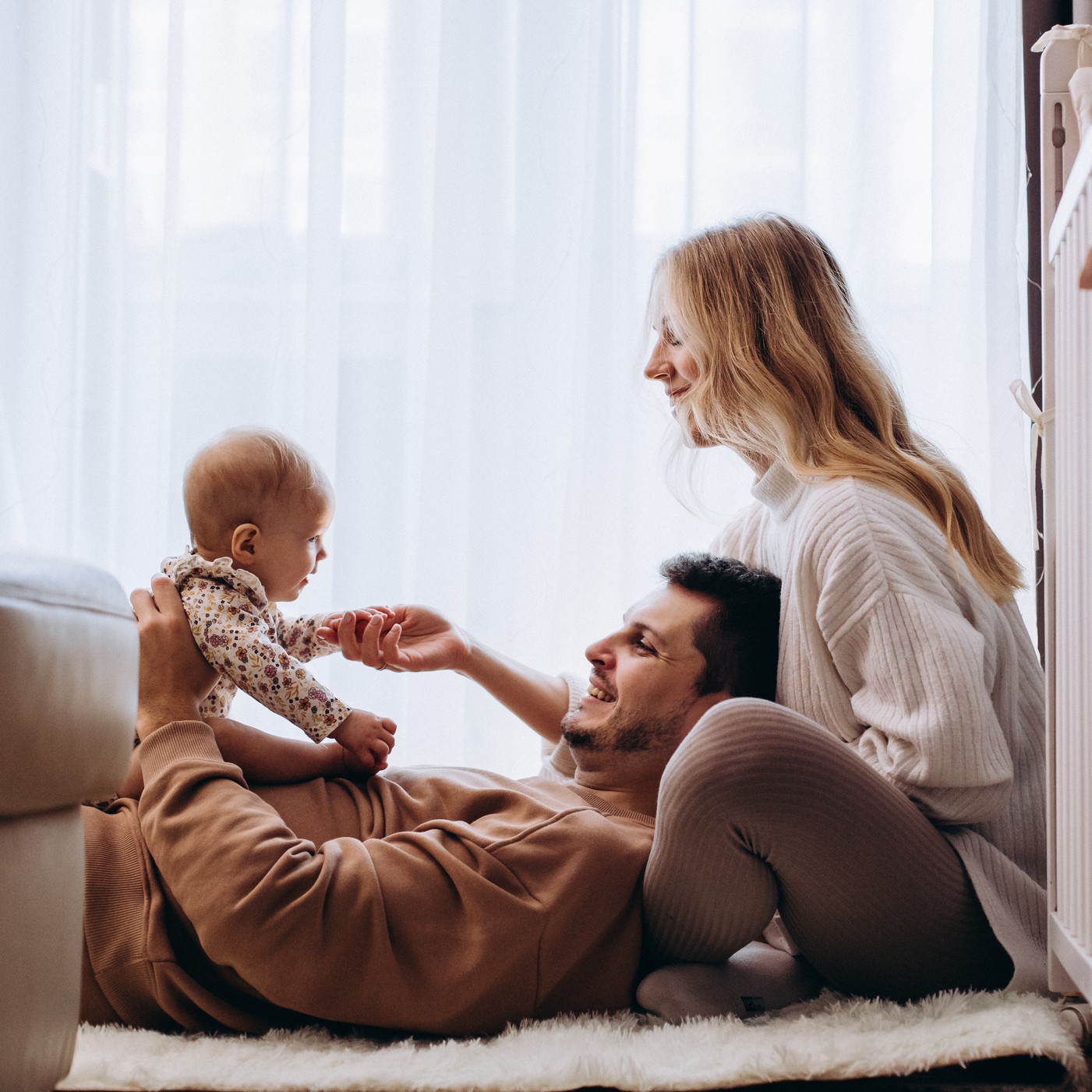 The cheerful parents playing with their little daughter in the bedroom on the floor at home